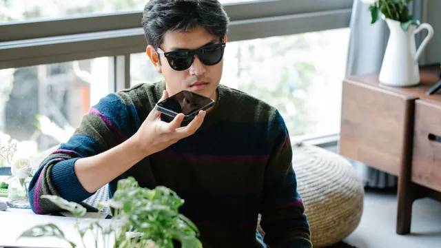 Man in sunglasses speaking into his smartphone to ask a voice assistant a question at home