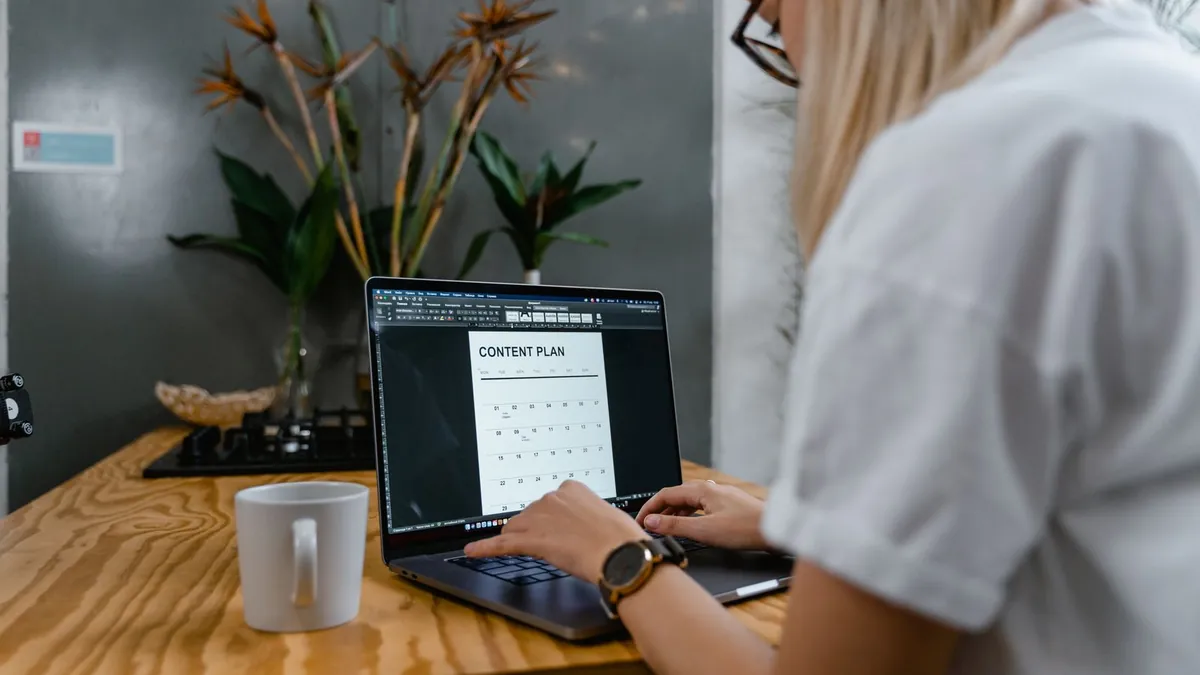 Woman typing on a laptop at a wooden desk while working on a content plan